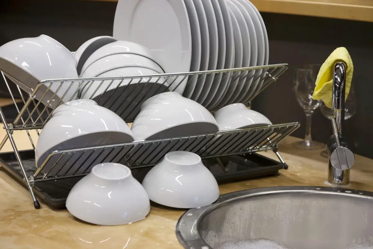 white plates and bowls on a dish drying rack on a countertop