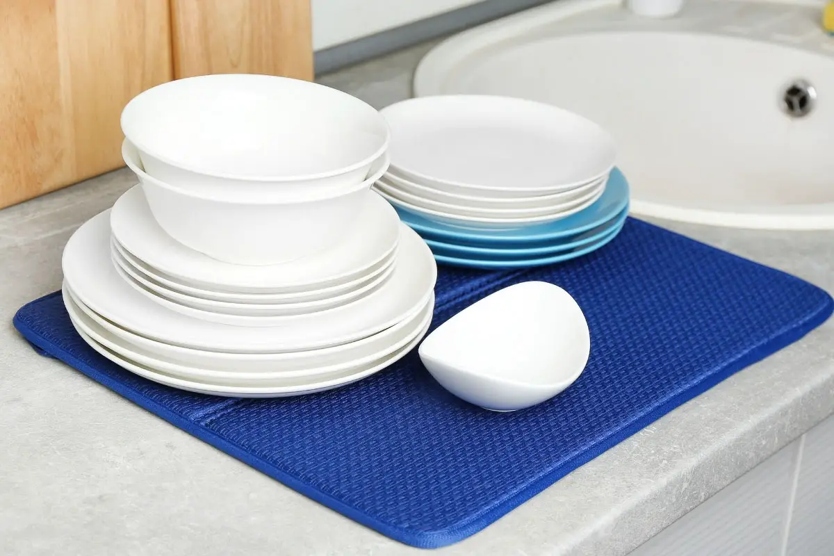 white dishes stack on a blue dish drying mat on a grey countertop