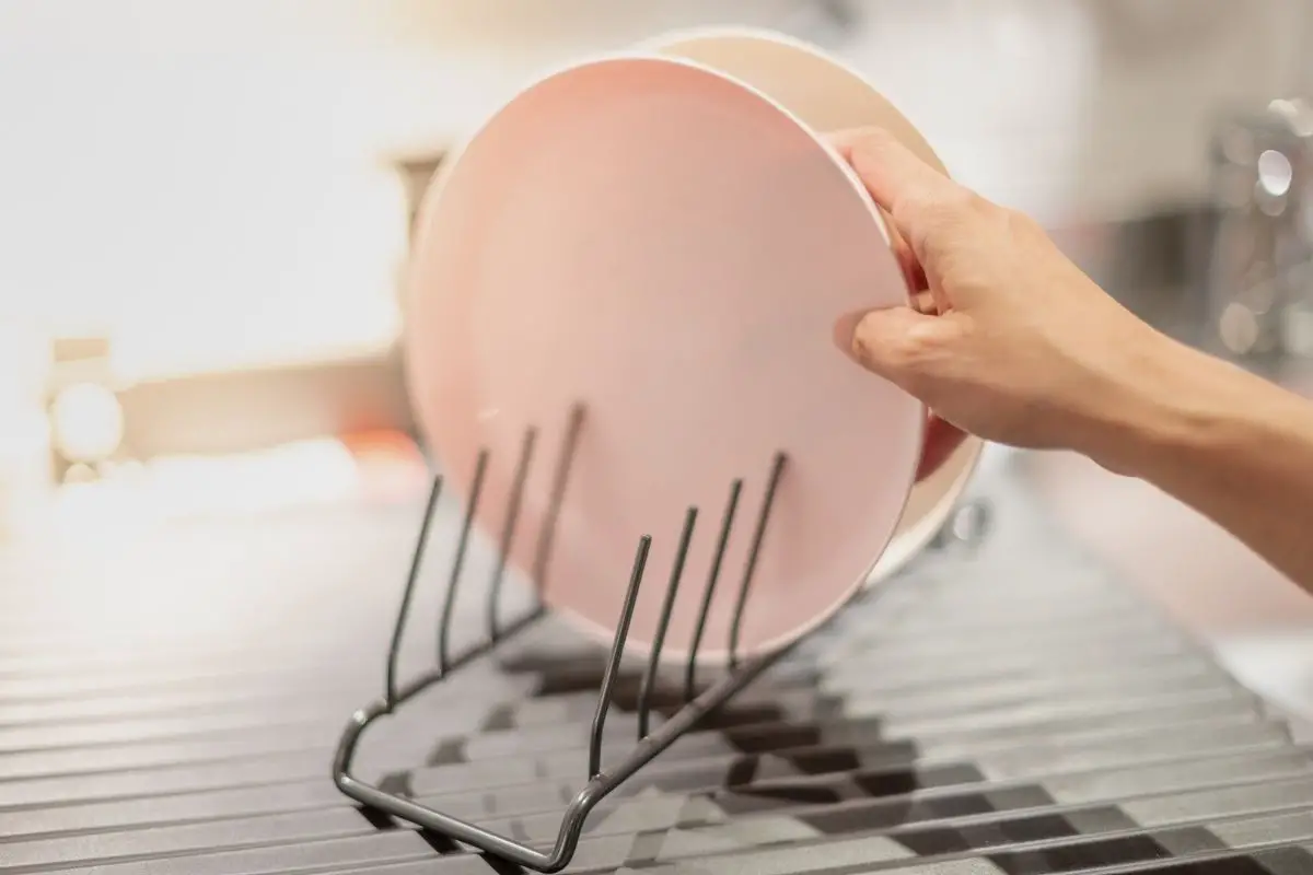 clean plates being placed on a metal dish drying rack